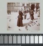 Schwarz-weißes, grinsendes Bild einer elegant gekleideten Frau, die Tauben füttert, zwei Männer stehen etwas weiter weg und beobachten sie